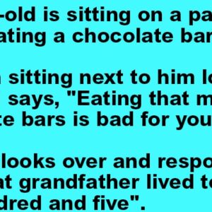 A 7-year-old is sitting on a park bench eating a chocolate bar.